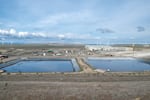 Rectangular ponds are surrounded by dry brush and a parking lot, with windmills visible in the distance.