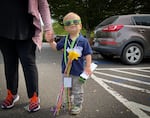 A small child decked out in swag, including sunglasses, a mini carboard bus, flowers and lanyards.