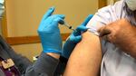 A person wearing a mask and gloves injects vaccine into the arm of a person with a rolled up sleeve who is also wearing a mask.