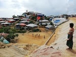 A Rohingya boy watches a game of chinlone, also known as caneball, a traditional sport from Myanmar. The rooftops of refugee homes in the distance are typically made of bamboo and tarpaulin.