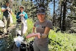 A female biologist smiles as she holds out a yellowhead bumblebee in her hand while she stands on a wooded trail with a small group of preseverationists.
