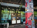 A windowed storefront with signs reading BLACK LIVES MATTER. There are portraits of George Floyd and Breanna Taylor behind the glass, and in chalk marker on the glass, the names of dozens of other people killed by police in recent years. A light pole in front of the restaurant is covered in mostly black-and-red stickers; a prominent one reads "FROM EACH ACCORDING TO ABILITY AND TO EACH BASED ON NEED".