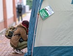 A person speaks to someone inside of a tent, camping on the sidewalk in downtown Portland in this Nov. 15, 2023 file photo. New rules will allow people to camp on public property if shelter beds aren't available, but it also prohibits people from blocking access to private property, using a propane heater and other activities.