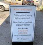 A picture of a sign posted in a parking lot. The sign reads: "No lines beyond this point. Find the landlord's security for line queing details. Please direct any questions to the property manager: Henry Hornecker," followed by two phone numbers, an email address, and several small logos.