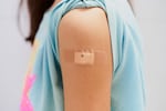 A girl's T-shirt sleeve is rolled up, revealing a bandage after receiving a vaccine in the upper arm.
