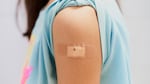 A girl's T-shirt sleeve is rolled up, revealing a bandage after receiving a vaccine in the upper arm.
