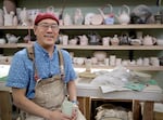 Ceramics artist and educator John Hasegawa sits in front of a wall of finished ceramics work from his students in his classroom at Mt. Hood Community College.
