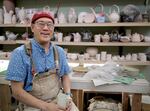 Ceramics artist and educator John Hasegawa sits in front of a wall of finished ceramics work from his students in his classroom at Mt. Hood Community College.