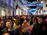People look up at Christmas lights as crowds stroll around downtown Lisbon's Chiado neighborhood, on Saturday, Dec. 23, 2023.