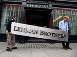 Two employees of the auction house Christie's bring down the Lehman Brothers corporate logo in London, England, on Sept. 24, 2010. Experts warn a U.S. debt default could spark another global financial crisis, similar to the one that hit in 2008. Lehman, an investment bank, was one of the high-profile casualties of that crisis over a decade ago.