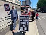 Multnomah County Chair Jessica Vega Pederson, right, and District Attorney Mike Schmidt hold signs announcing the county's lawsuit against fossil fuel companies in Portland, Ore., Thursday, June 22, 2023. The county is suing 17 oil and gas companies, alleging the burning of their products contributed to a deadly heat wave in 2021.