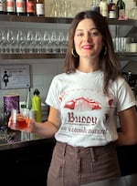 Bartender Nora Furst poses behind the bar at Grape Ape with a booze-free spin on a classic Italian cocktail, August 17, 2023. Dubbed the NEWgroni, Furst says she's found enjoyment and exploration in the non-alcoholic spirits world.