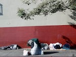 A person kneels on the sidewalk as another person sleeps in the Skid Row community on Dec. 14, 2022 in Los Angeles, California. The Skid Row community is home to thousands of people who either live on the streets or in tents or makeshift shelters.