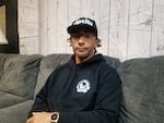 A man wearing a black hoodie, glasses and a black baseball cap with the RipCity logo sits on a couch