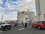 Vehicles, emergency personnel and several onlookers gather in a parking lot across the street from a tall, charred building with smoke coming out of it.