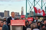 In this photo, Canadian Prime Minister Mark Carney stands outdoors behind a lectern during an election rally in Windsor, Ontario, on April 26, 2025. He's surrounded by people, two of whom hold signs saying "Never 51."