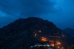 A view of flaming torches being carried about a third of the way up a mountain at twilight.