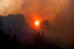 The sun appears orange and hazy, visible between mountain peaks and through a cloud of thick smoke.