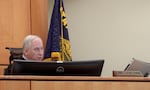 A man in judge's robes looks out from the bench as he listens to an out of frame attorney speaking remotely.
