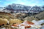 snow dusts layered mountain in background and red, yellow and tan hills in the foreground