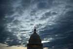 The U.S. Capitol dome is shown at dusk with light filtering through scattered clouds.