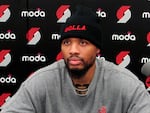 A man sits down at a press conference in a black beanie and grey sweatshirt.