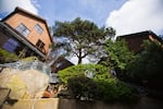This photo shows the Boulders development in Seattle. Several multistory houses with wooden exteriors surround a large tree, and a waterfall flows over large rocks.