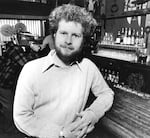 A black and white portrait of Randy Shilts leaning against a bar.