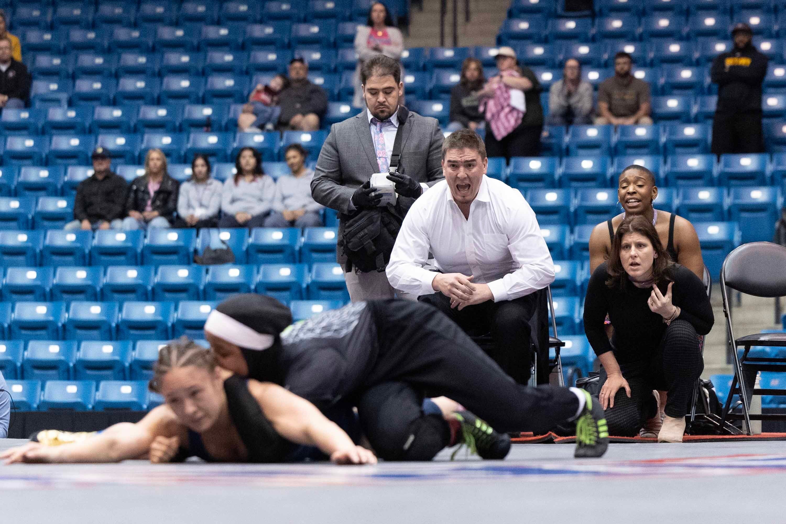 Associate head wrestling coach Christian Flavin (center) and head coach Ashley Flavin (right) watch intently as Zaynah McBryde competes.