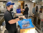 Jackson Walker, left, and Benjamin Fisher, right, prepare some chicken legs on Dec. 3, 2021, to cook in the oven for dinners that Meals On US PDX will later deliver to area shelters. Mickey Leonardini observes from the back of the kitchen.