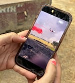 A woman holding a phone showing a photo of a plane dropping bright red fire retardant on grassland.