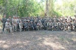 Wearing camouflage-print uniforms, U.S. and Filipino troops stand or kneel in a long row for a photo during annual Balikatan exercises. Some are holding firearms.