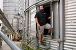 Ian Stamy stands in the doorway of one of his grain silos on August 12. The silo is made from silver corrugated metal. Stamy is wearing boots, light-colored shorts and a dark T-shirt.
