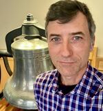 A man stands in front of a large silver bell.