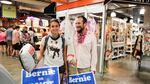Vanessa Perez, left, of Florida, and Niko Klein, right, of San Francisco, are decked out in pins, stickers, signs and a flag showing their support for Bernie Sanders in the Reading Terminal Market.