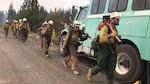 Firefighters walk carrying gear and holding protective equipment.