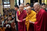 Tibetan spiritual leader the Dalai Lama, in yellow robe, is helped by attendant monks as he arrives to preside over an event during which Tibetan exiles prayed for his longevity, a day before his 90th birthday, in Dharamshala, India, Saturday, July 5, 2025.\
