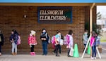students lining up outside a brick building with a large sign reading ellsworth elementary