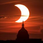This 2021 photo shows a partial solar eclipse in which the sun appears as a large crescent in the orange-red sky behind the U.S. Capitol.