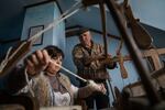 Lubov Hychka demonstrate how to weave the hunia fabric while Vasyl Hychka (unrelated), who takes care of the property where the loom is housed, helps with the rickety old machine.