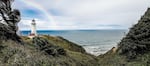 A rainbow curves above a coastal lighthouse, with the ocean in the background.