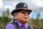 Ed Edmo, Shoshone-Bannock, wears a black hat with a beaded rim, sunglasses, a purple collared shirt and a black vest.