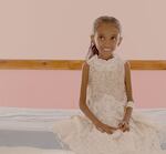 A very thin girl wears a white dress and smiles while sitting on a bed.