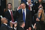 Elon Musk stands as he is recognized by President Trump during the latter's address to a joint session of Congress on Tuesday. Musk is holding his hand at his forehead in a salute gesture, and he's wearing a blue suit with a blue tie. He's surrounded by other attendees of the address, who are applauding.