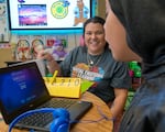 Third-grade teacher Kayla Davidson, left, works with a student in class at Fern Hill Elementary School in Forest Grove, Ore., Nov. 9, 2023. Davidson utilizes the PAX Good Behavior Game in her classroom to help students identify and encourage positive “PAX” behaviors  and avoid “spleems,” indicated on the yellow scorecard, as part of daily classroom management.