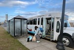 A bus with a woman in a jean jack lifting up her backpack