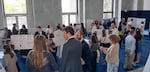 A crowd of people stand in a room with posters displayed on easels with a science fair feel to it.