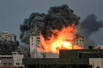 People standing on a rooftop watch as a ball of fire and smoke rises above a building in Gaza City.