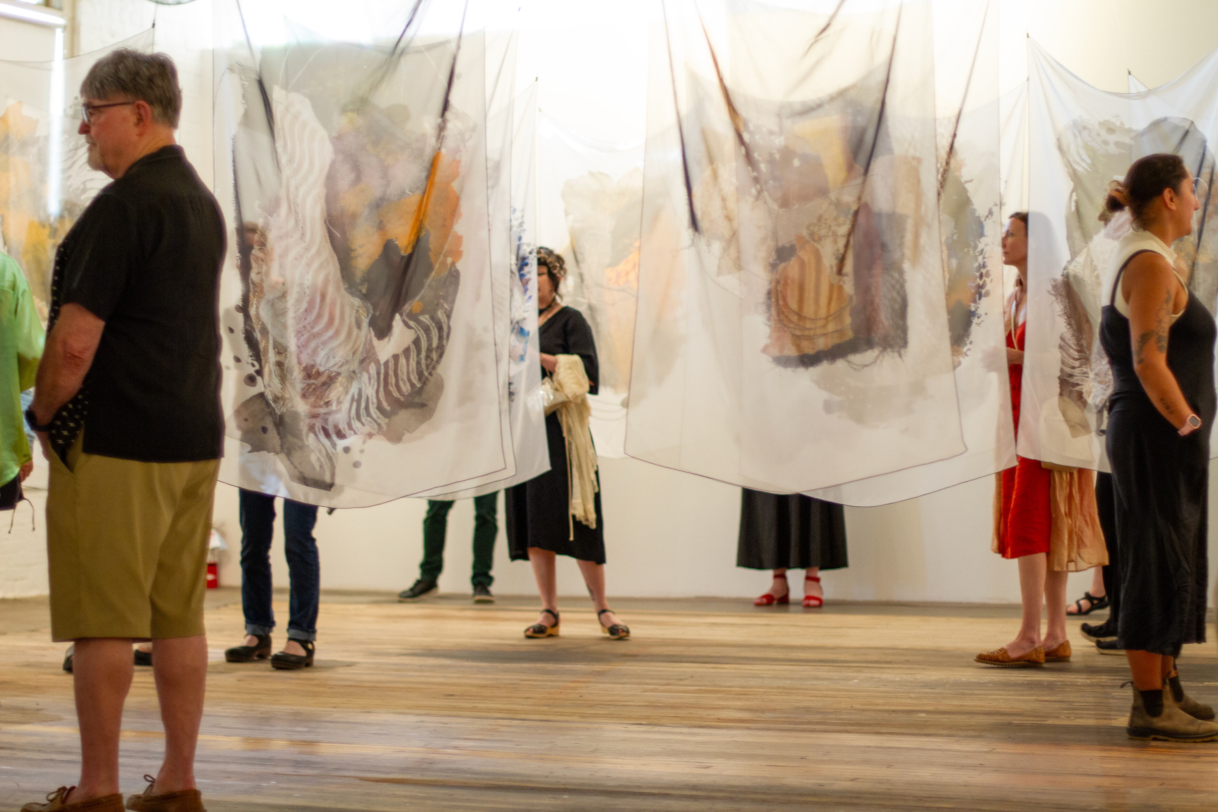 Attendees interact with more than a dozen art pieces printed on silk chiffon fabrics that hang from the ceiling of the Center for Native Arts & Cultures building during the grand opening of the 
