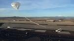 The partially inflated high-altitude balloon drifts skyward over a crane truck on the runway.  When fully extended and vertical, the truck will release the ESA module without it hitting the ground.